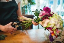 Обрізане зображення жіночого флориста, що обрізає квіткові стебла в її квітковому магазині — стокове фото