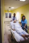 Blurred view of doctor and nurse pushing senior patient on stretcher in hospital corridor — Stock Photo