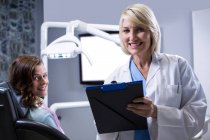 Dentista sorridente com prancheta e paciente na clínica odontológica — Fotografia de Stock