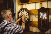 Vista trasera del horólogo reparando un reloj colgado en la pared en el taller - foto de stock