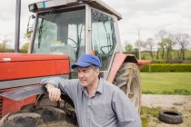 Фермер опирается на трактор на поле — стоковое фото