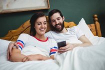 Пара використовує мобільний телефон на ліжку в спальні — стокове фото