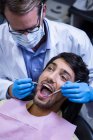 Dentista examinando um paciente com ferramentas na clínica odontológica — Fotografia de Stock