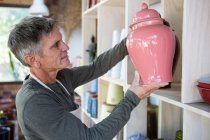 Gros plan du potier masculin qui place le pot sur une étagère dans un atelier de poterie — Photo de stock