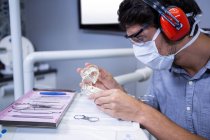 Dentiste masculin regardant le modèle de bouche avec des loupes dentaires — Photo de stock