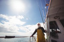 Baixo ângulo de visão do pescador segurando haste de pesca e olhando para a vista do barco — Fotografia de Stock