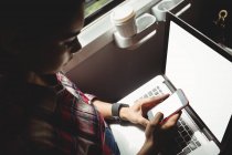 Jovem usando telefone inteligente com laptop enquanto está sentado no trem — Fotografia de Stock