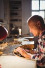 Aufmerksame Goldschmiedin formt Metall mit Säge in Werkstatt — Stockfoto