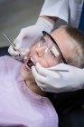 Стоматолог осматривает молодого пациента с помощью инструментов в стоматологической клинике — стоковое фото