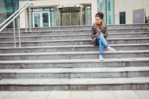 Full length of woman holding phone while sitting on steps — Stock Photo