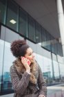 Счастливая женщина разговаривает по телефону, сидя напротив здания — стоковое фото