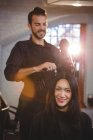 Портрет улыбающейся женщины, высушивающей волосы феном в парикмахерской — стоковое фото