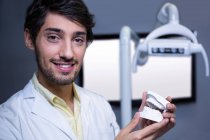Dentiste souriant tenant un modèle de bouche à la clinique dentaire — Photo de stock