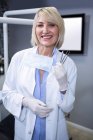 Retrato del dentista sonriente sosteniendo herramientas dentales en la clínica dental - foto de stock