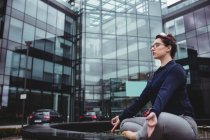 Lunghezza completa della donna d'affari che fa yoga contro edificio per uffici — Foto stock