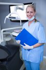 Smiling dental assistant holding clipboard in dental clinic — Stock Photo