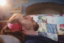 Молодий чоловік слухає музику, розслабляючись на дивані вдома — стокове фото
