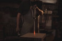 Section médiane du forgeron tenant une tige métallique rouge chaude avec des pinces à l'atelier — Photo de stock