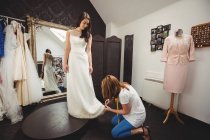 Mujer probándose el vestido de novia en el estudio con la ayuda del diseñador creativo - foto de stock