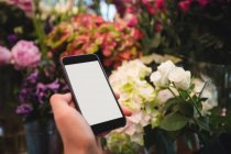 Mano de florista femenina sosteniendo teléfono móvil en la floristería - foto de stock