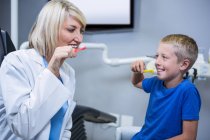 Dentista sorridente e paciente escovando os dentes na clínica odontológica — Fotografia de Stock