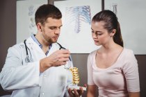 Fisioterapeuta explicando columna vertebral a paciente femenina en clínica - foto de stock