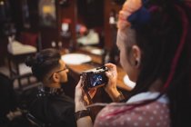 Peluquero femenino tomando fotos del cliente de la cámara digital en la peluquería - foto de stock