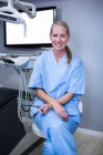 Assistente dentário sorridente sentado ao lado de equipamentos odontológicos na clínica odontológica — Fotografia de Stock