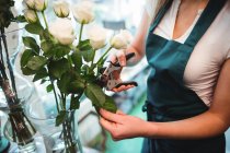 Обрезанное изображение женщины-флористки, стригущей листья цветов в цветочном магазине — стоковое фото