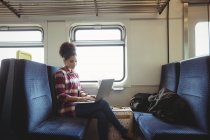 Mujer usando el ordenador portátil mientras está sentado en tren - foto de stock