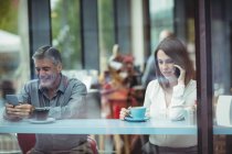 Mensajería de texto masculina mientras la mujer habla en el teléfono móvil en la cafetería - foto de stock
