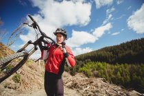 Motociclista che trasporta bicicletta in montagna contro il cielo — Foto stock