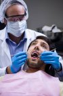 Dentiste examinant un patient avec des outils à la clinique dentaire — Photo de stock