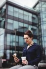 Young woman using mobile phone against office building — Stock Photo