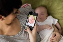 Мама фотографирует своего ребенка со смартфоном в гостиной дома — стоковое фото