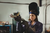 Saldatore donna esaminando pezzo di metallo in officina — Foto stock