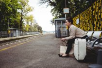 Full length of woman waiting while sitting on bench at railroad station — Stock Photo