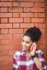 Lächelnde hübsche Frau telefoniert, während sie gegen Ziegelmauer steht — Stockfoto