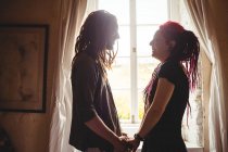 Smiling young couple holding hands against window at home — Stock Photo