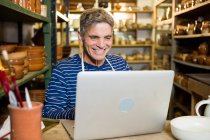 Счастливый мужчина гончар с помощью ноутбука в мастерской керамики — стоковое фото