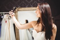 Mujer tomando selfie mientras se prueba el vestido de novia en el estudio - foto de stock
