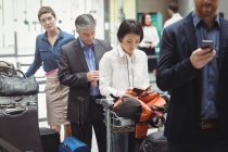 Passengers waiting in queue at a check-in counter with luggage inside the airport terminal — Stock Photo
