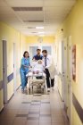 Лікар і медсестра штовхають старшого пацієнта на ноша в лікарняному коридорі — стокове фото