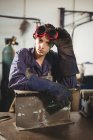 Porträt einer Schweißerin, die mit einem Metallstück in der Werkstatt steht — Stockfoto