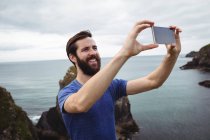 Man taking selfie from mobile phone on cliff — Stock Photo