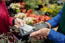 Imagem cortada de mulher fazendo pagamento com cartão de crédito para florista no centro de jardim — Fotografia de Stock