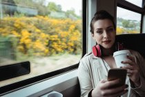 Портрет жінки, яка використовує мобільний телефон, сидячи в поїзді — стокове фото