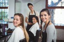 Portrait of smiling hairdressers working on clients at hair salon — Stock Photo