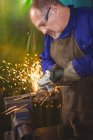 Welder sawing metal with electric tool in workshop — Stock Photo