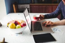 Обрезанные изображения пары с помощью ноутбука в то время как фрукты и цифровой планшет на столе дома — стоковое фото
